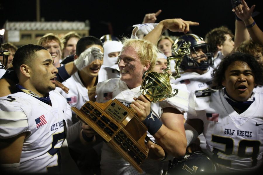 Gulf Breeze football players celebrate on the field with the Publix Beach Bowl trophy after beating Navarre 38-26